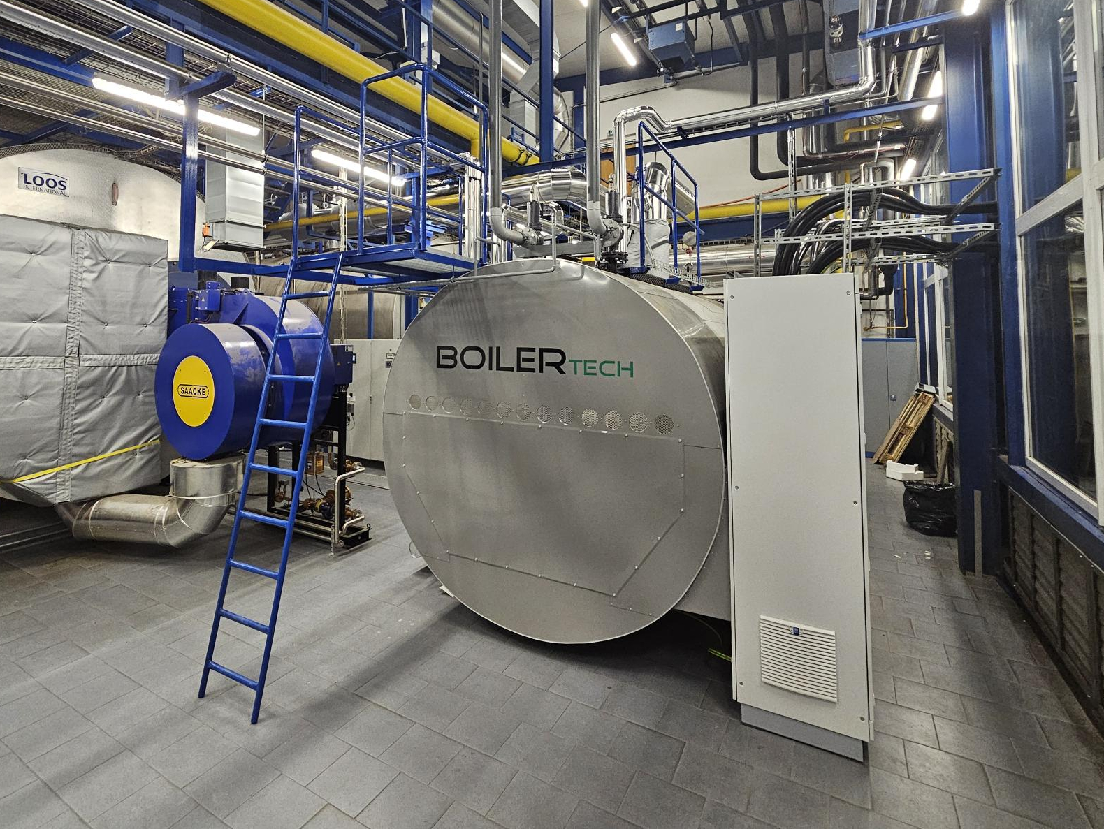 Large industrial Boilertech boiler in a boiler room with a blue ladder and piping
