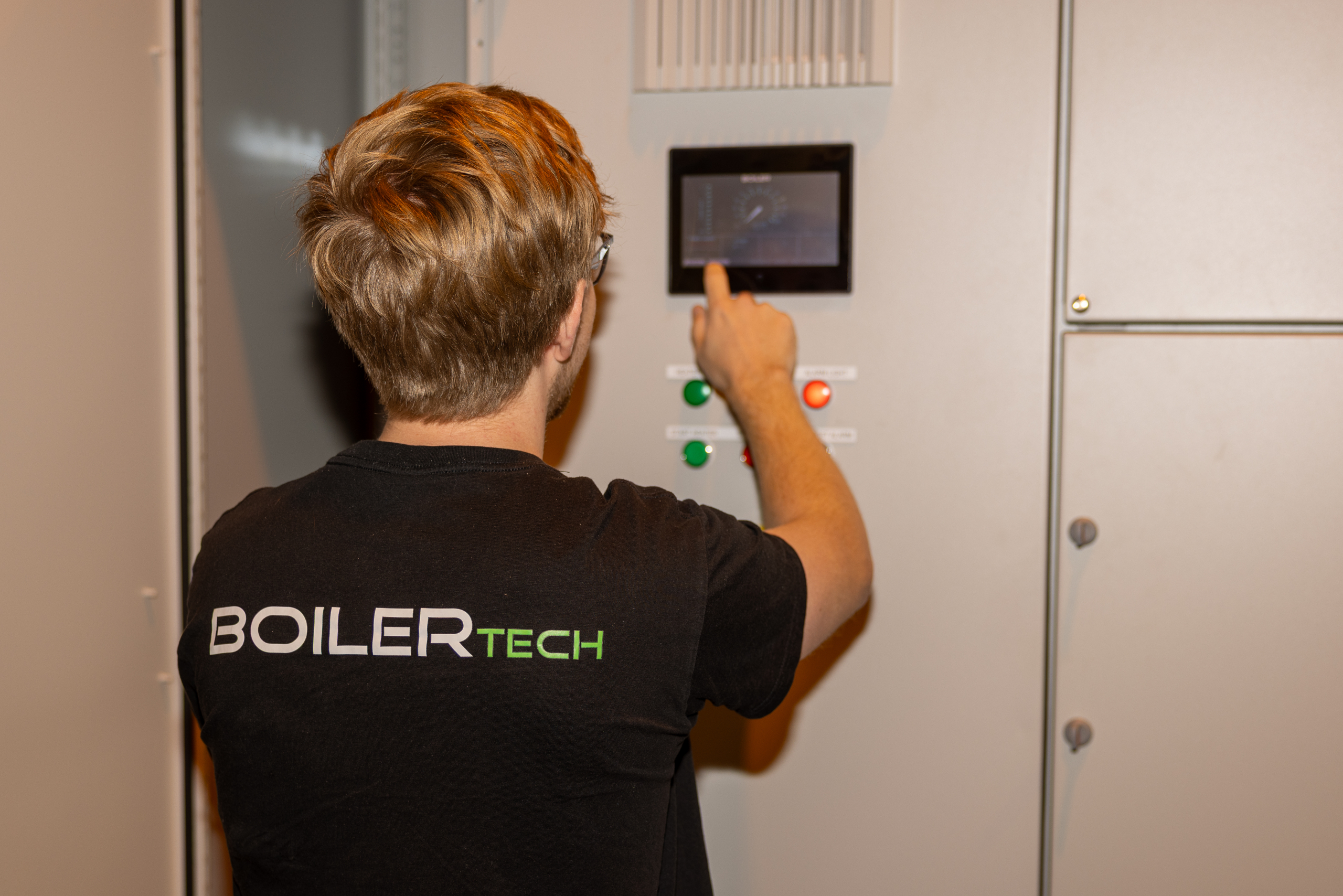 A Boilertech technician operates a touchscreen on a control panel